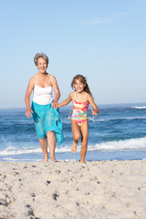 Naklejka premium Grandmother Running With Granddaughter Along Sandy Beach