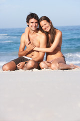 Young Couple Relaxing On Beach Wearing Swimwear