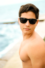 Young muscular man in sunglasses on the seashore