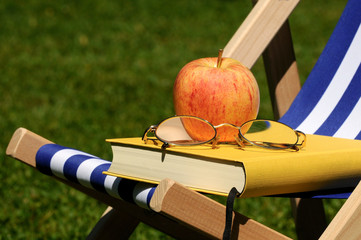Buch, Brille und Apfel auf Liegestuhl