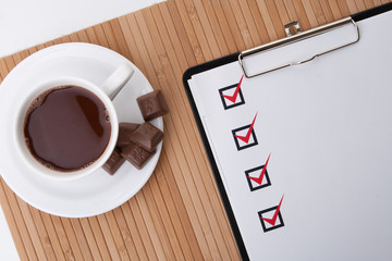 Cup of hot coffee and checklist on clipboard