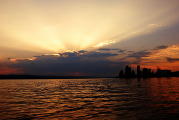 beautiful sunset on lake with sunrays rising behind the clouds