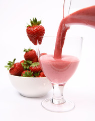 Strawberries and a strawberry shake being poured into glass