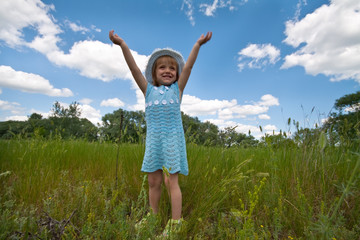 Cute little girl rising hands in a grass field