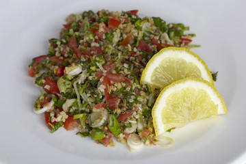 Lebanese Tabbouleh with two lemon slices on a white plate.