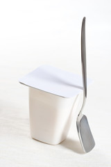 Cream yogurt in plastic box with spoon on white background