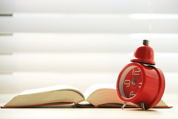 Isolated open book with red  alarm clock on of the table .