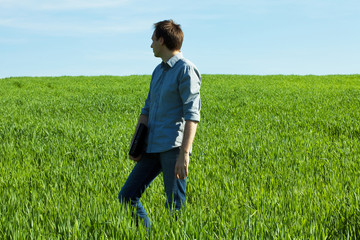 young man standing with a laptop in the green field