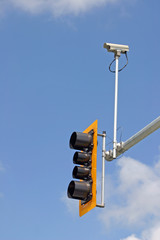 Security camera with traffic light and blue sky background.