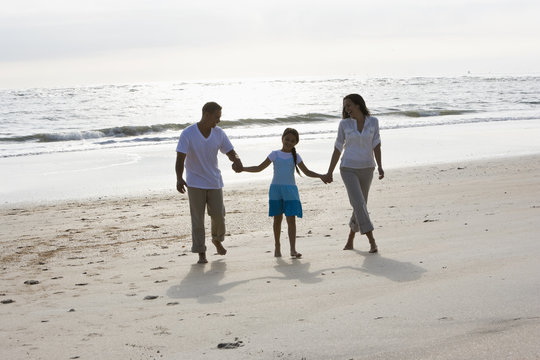 Hispanic family holding hands walking on beach