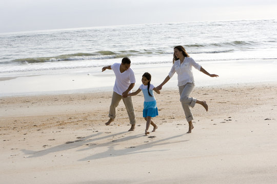 Hispanic family holding hands skipping on beach