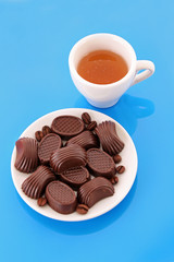 Assorted chocolate candies and cup of tea on blue background
