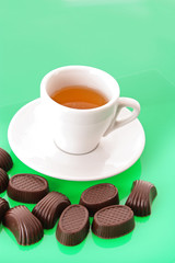 Assorted chocolate candies and cup of tea on green background