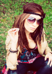 Beautiful young hippie girl sitting in the grass with cigarette