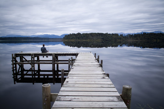 Man fishing in a lake off the end of a wooden jetty in forest