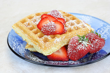 Waffles  garnished with strawberry slices and powdered sugar.