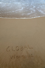 Fototapeta premium Global warming written in the sand at beach with rising wave
