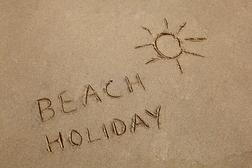Beach Holiday written in the sand with a sun symbol.