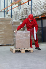 worker wrapping box on wooden pallet in warehouse