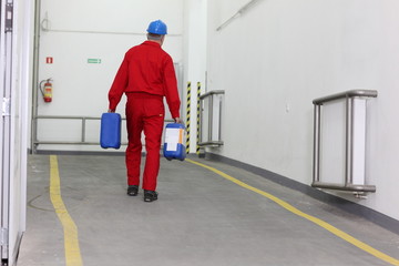 Back view of a factory worker carrying  bottles of chemicals