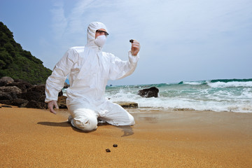 Worker in a protective suit examining pollution at the beach