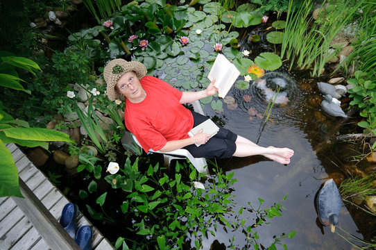 Frau sitzt mit Büchern im Biotop