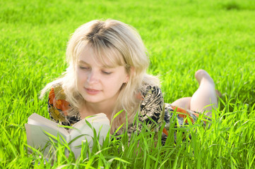 Young beautiful girl reading a book outdoor in green grass