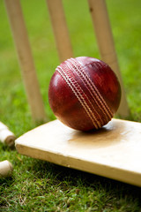 Red leather cricket ball on grass with stumps