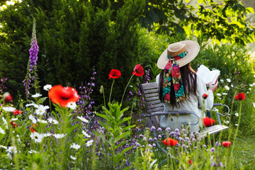 woman with straw hat reading a book within summer flowers