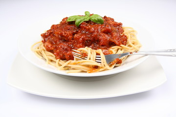 Spaghetti bolognese on a plate and a fork decorated with basil