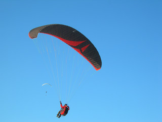 A paraglider flying in the sky with his red and black paraglide