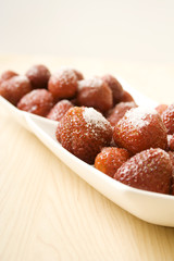 On the table is a plate of strawberries sprinkled with sugar