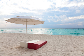 Two beach beds under umbrella with aqua green ocean