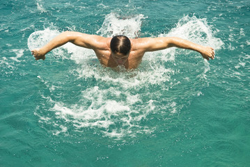 man swimming butterfly stroke in blue water.