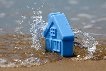 Toy plastic house on the sand washes wave