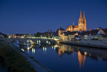 Altstadt Regensburg, beleuchteter Dom und Steinerne Brücke zur blauen Stunde mit Reflektion in...
