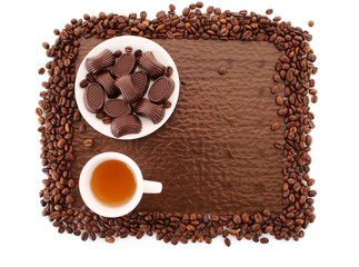 Assorted chocolate candies and cup of tea on brown background
