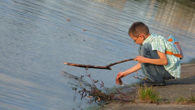 boy sitting on coast and beats by stick on water surface