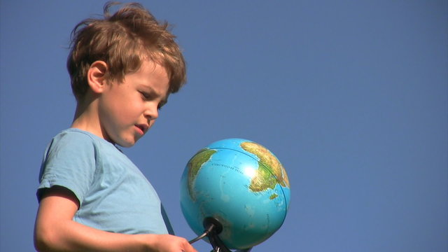 boy stands and looks at terrestrial globe