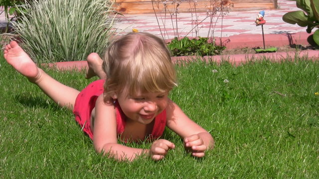 little girl lying on grass in outlet and dangles legs