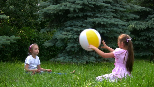 two girls sits on grass in summer park and plays