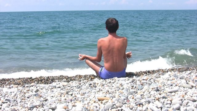 man sitting on beach in pose of lotus and looks at sea