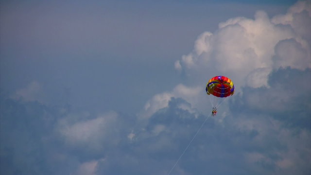 parasailing two humans on parachute flying in sky