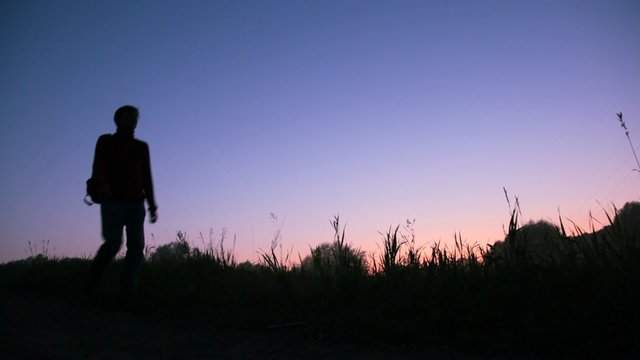 travaler with rucksack walks against sunset sky
