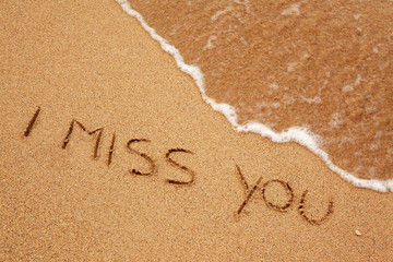 I miss you written in the sand with finger with wave rolling