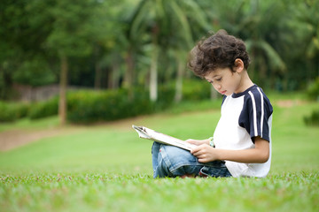 Naklejka na ściany i meble Young boy enjoying his reading book in outdoor park