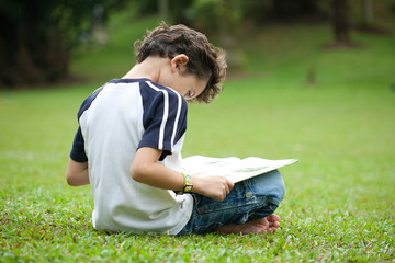 Young boy enjoying his reading book in outdoor park