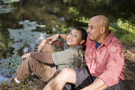 Portrait Hispanic Father And Son Outdoors By Pond