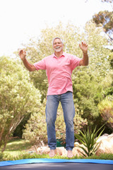 Senior Man Jumping On Trampoline In Garden