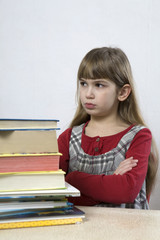 little cute sad girl with a pile of book sitting at table.